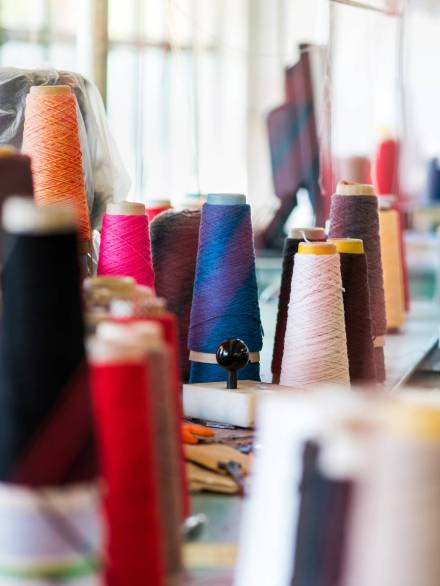 Multiple reels of cashmere wool or yarn in assorted colors on workbenches in a knitwear factory with focus to a stack of spools on a table in the center