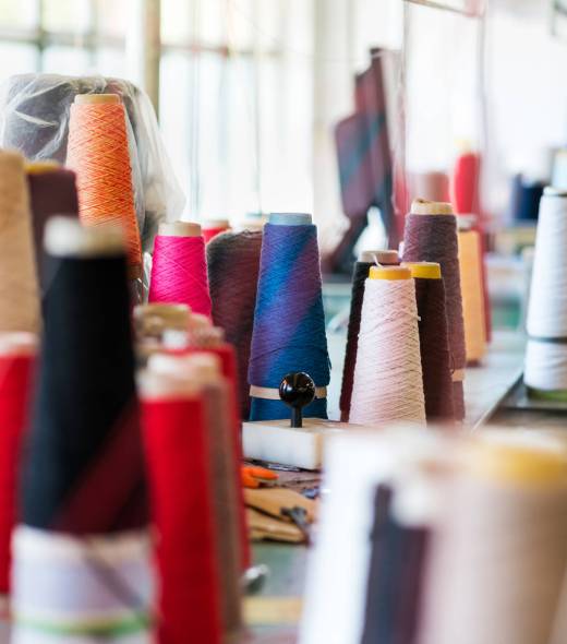 Multiple reels of cashmere wool or yarn in assorted colors on workbenches in a knitwear factory with focus to a stack of spools on a table in the center